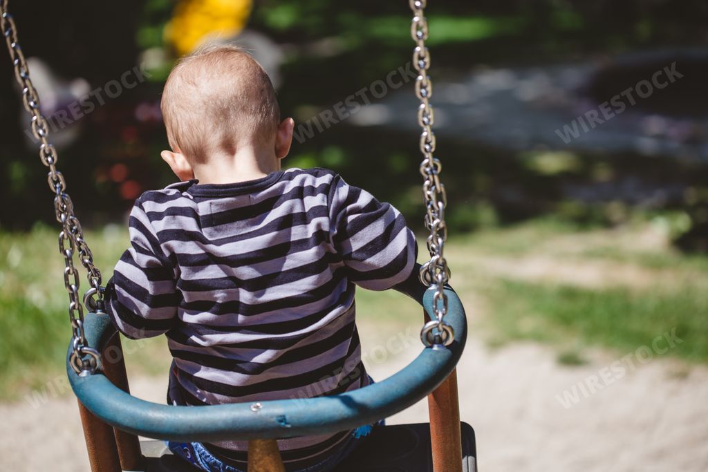 A shallow focus shot of a child sitting on a swing on the playground of a park