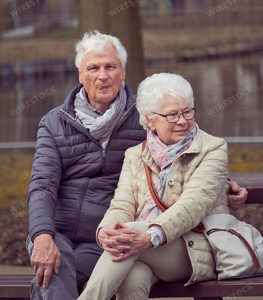 A vertical shot of a cute adult couple sitting on a bench in the park.