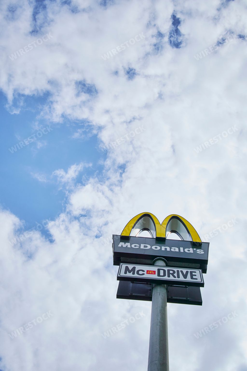 A low-angle vertical shot of the logo of a fast food restaurant under a blue cloudy sky in Germany