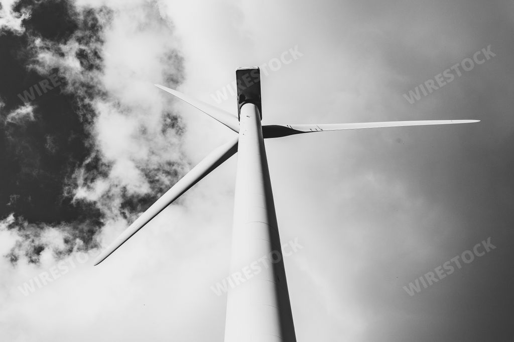 A grayscale low angle shot of a single windmill for electric power production with a cloudy sky behind