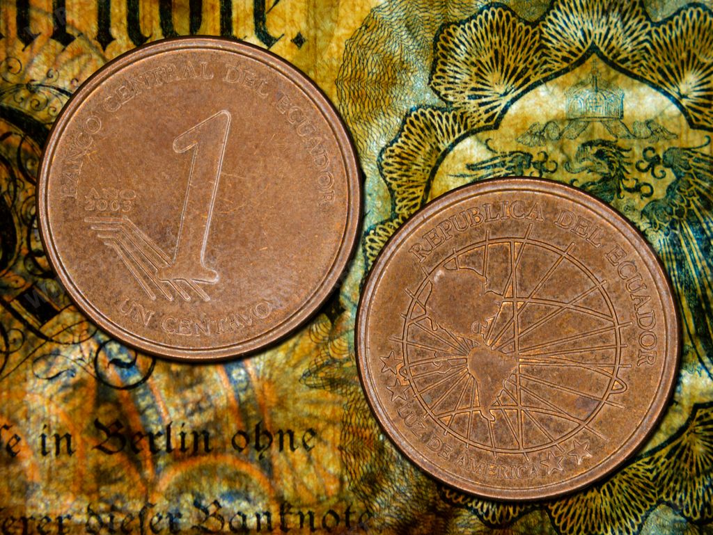 A close-up of two Ecuadorian centavo coins on a colorful banknote background