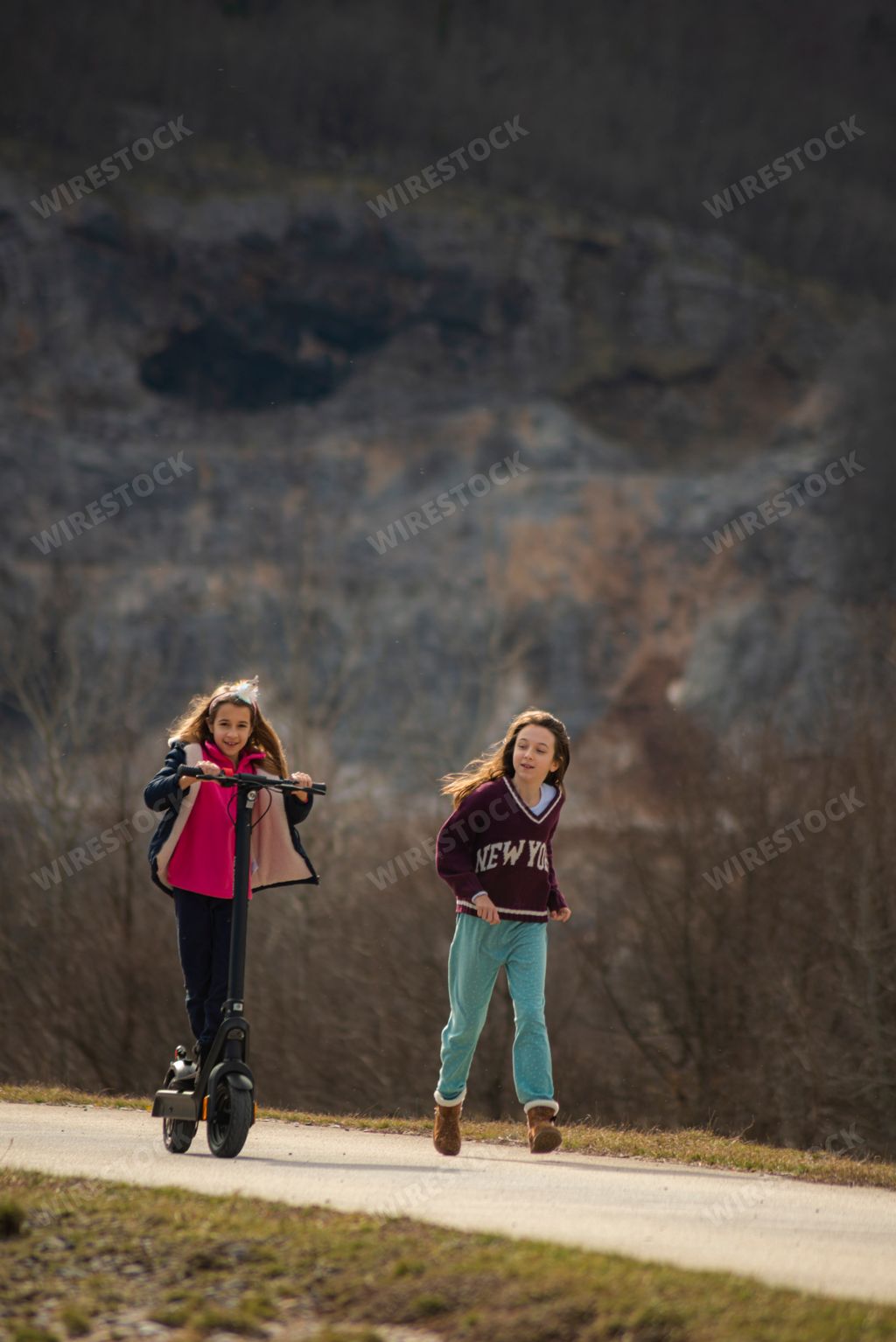 The two girls strolling and riding a scooter together