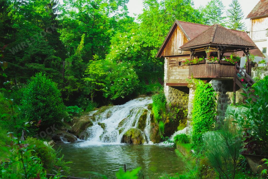 A house with a small waterfall pouring down to river surrounded by trees