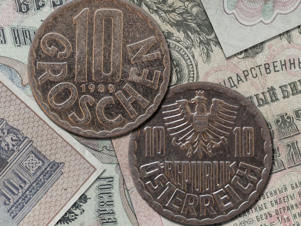 A closeup of an old Austrian schilling coin (10 groschen) on the banknotes background