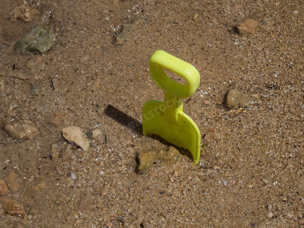 A top view closeup of a tiny yellow beach toy plastic shovel in the sand on the beach