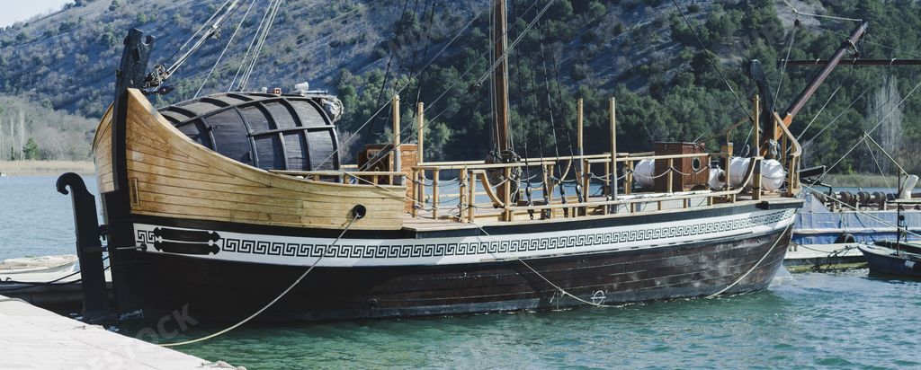 a large wooden ship docked on a port with green water - green hills background