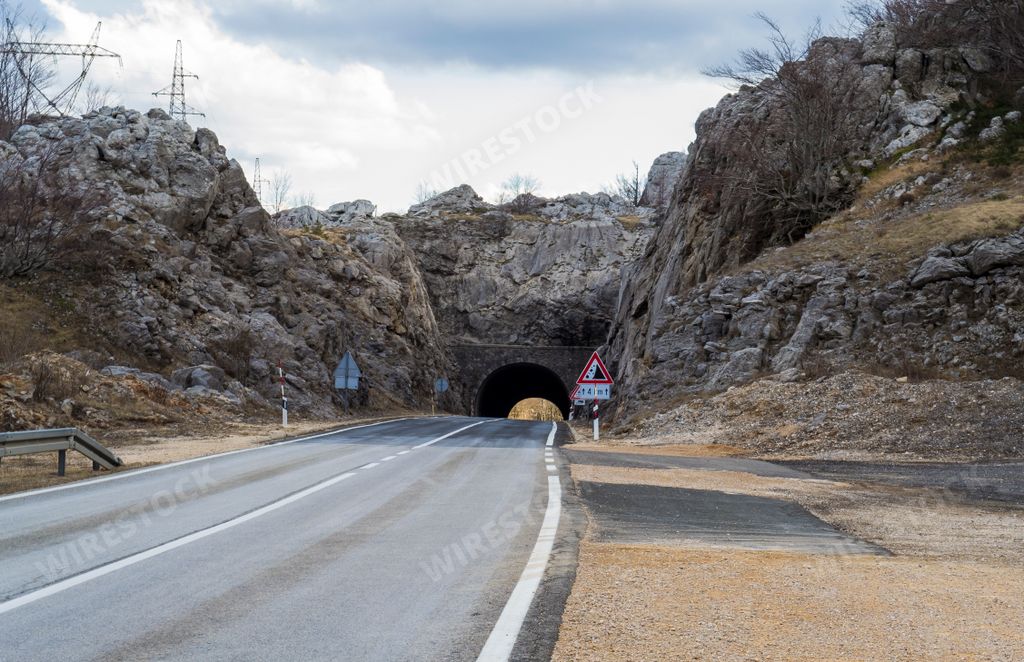 A beautiful shot of a road tunnel with road signs on the side with a cloudy gray sky in the background