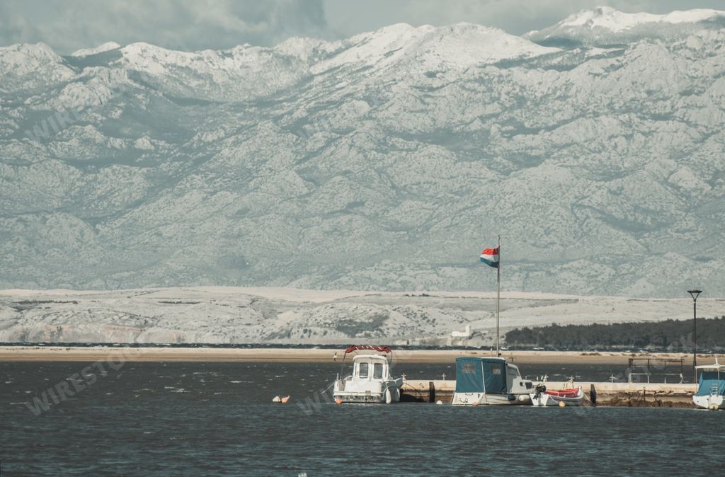 A port with boats with a flag of Netherlands and snowy mountains