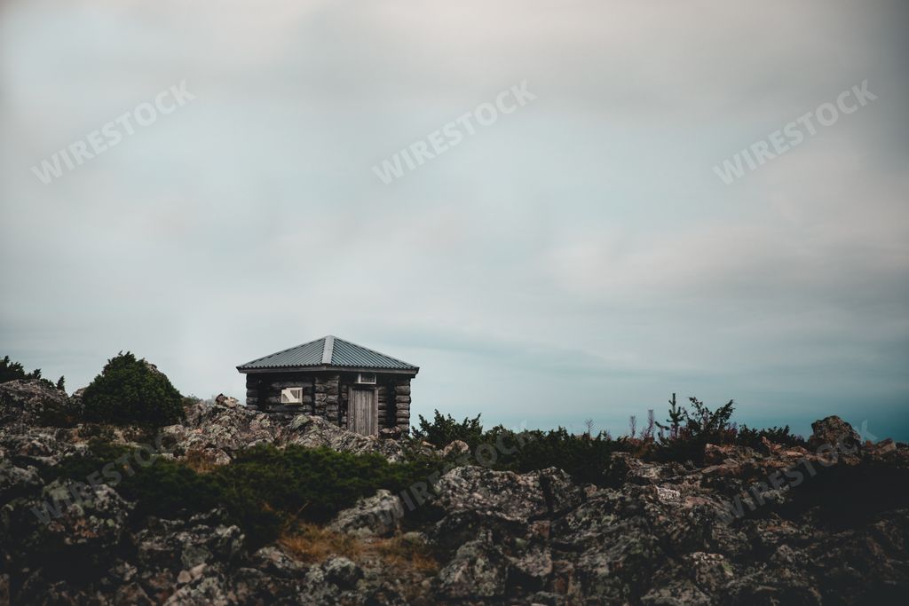 A small wooden house on a rock cliff in the countryside under a cloudy sky