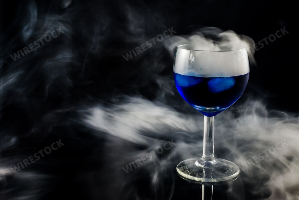 A closeup shot of a wine glass filled with blue liquid while smoking