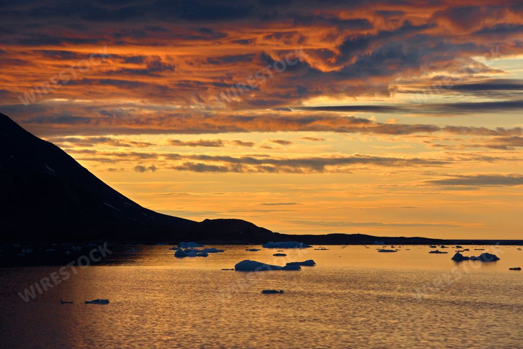 The silhouette of the side of a mountain against a beautiful sunset sky over the waters of Svalbard in Norway