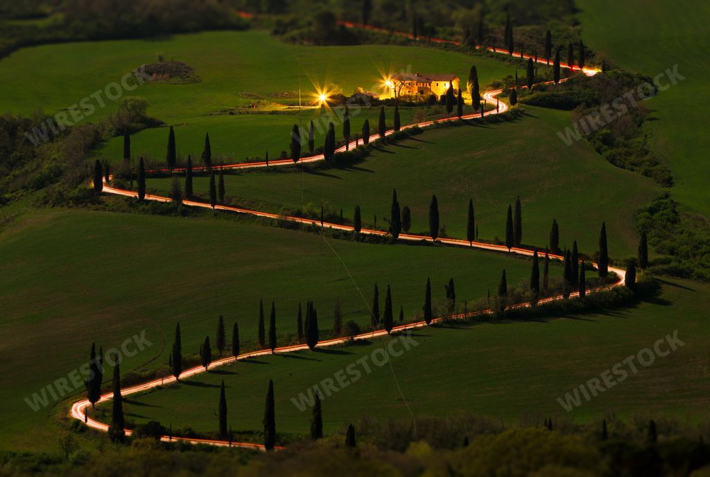 A landscape of a curvy road on a hill covered in greenery in the evening in Tuscany, Italy