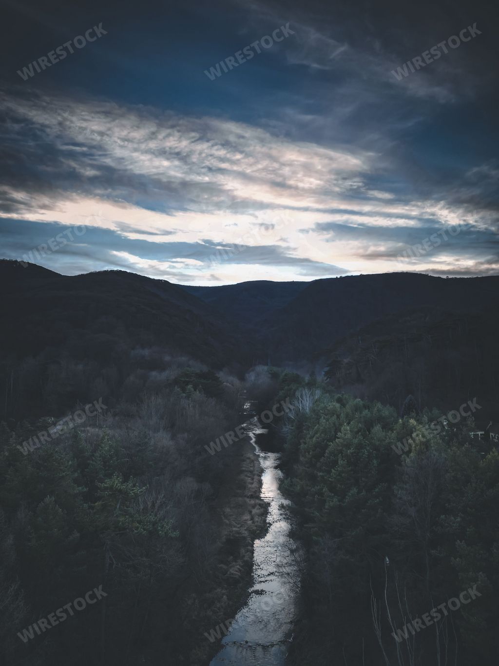 A scenic landscape of a hillside with a river cascading down towards the majestic mountains