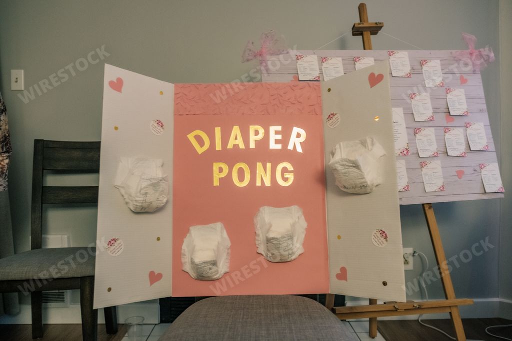A baby shower game set up of diaper pong with four diapers on a pink and white board