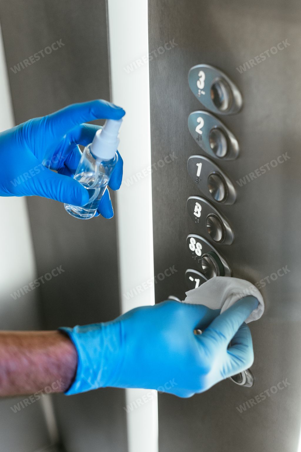 A vertical shot of a person sanitizing the elevator buttons