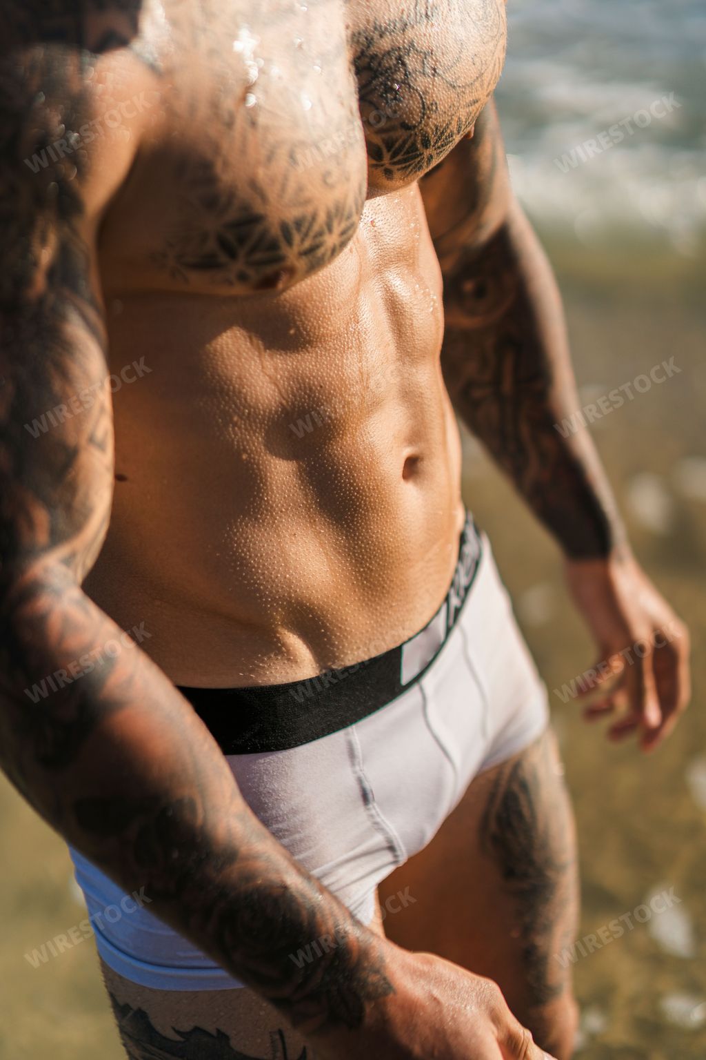 A closeup of a handsome fit tattooed Caucasian man in underwear in the sea.