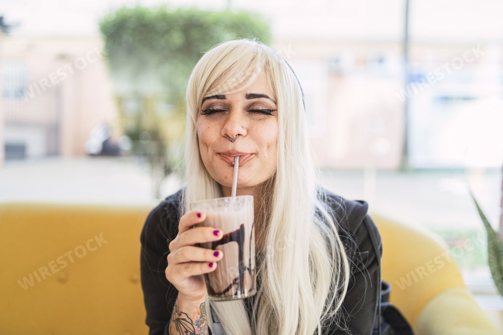 A young blonde female with piercings and tattoos drinking milkshake