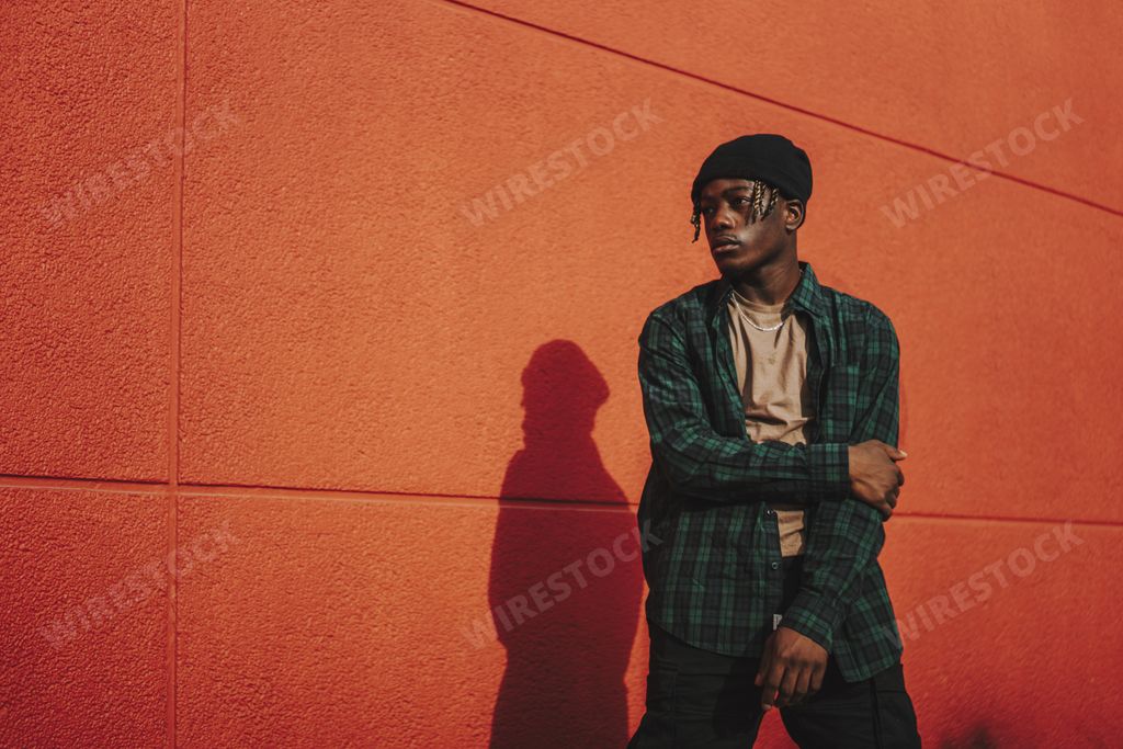A handsome stylish Spanish man posing on a red wall background on a sunny day