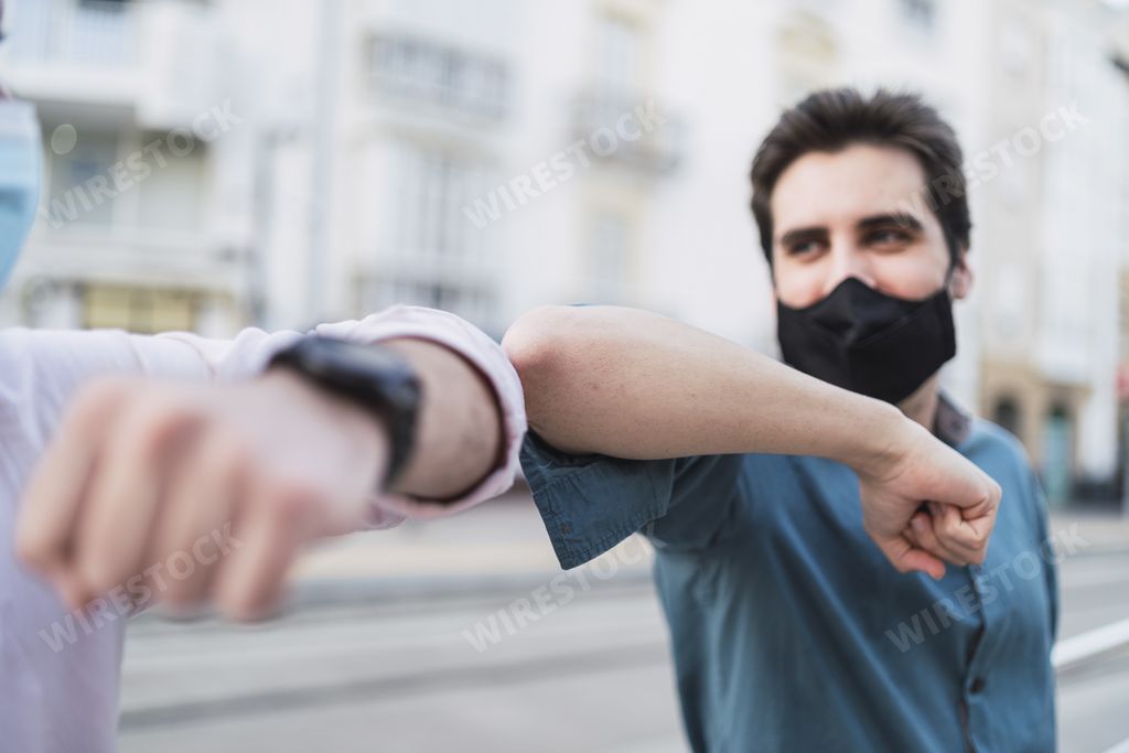 A handsome Spanish man wearing a mask and greeting his friend with elbows - new normal concept