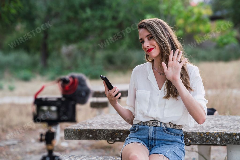 A young Spanish female blogger using her phone and recording herself with a DSLR camera in a park