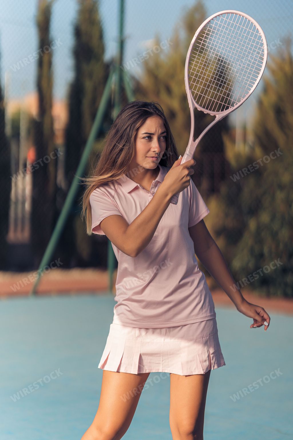 A vertical shot of a young female in pink athleisure playing tennis with a pink racket on a court