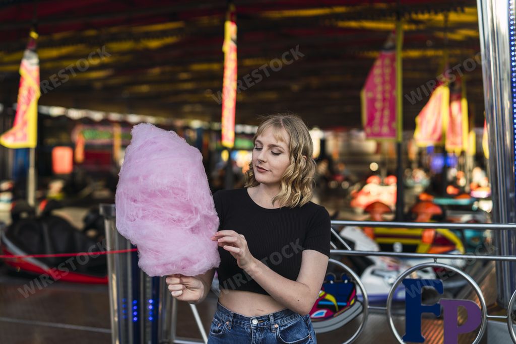 A blonde Spanish female eating cotton candy in an amusement park