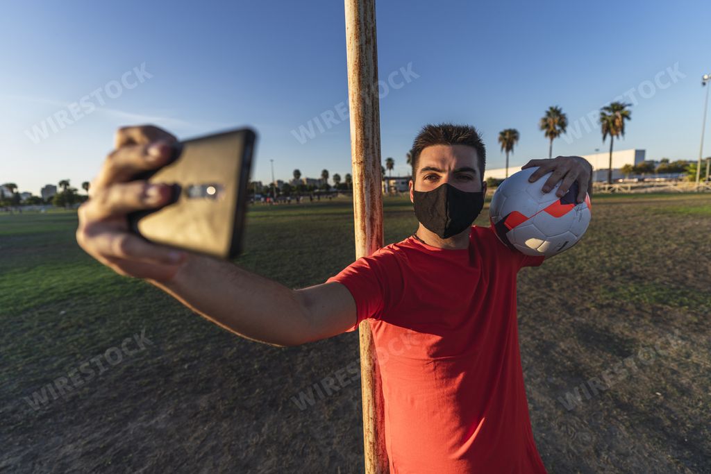 A soccer player in a black mask making a selfie with a ball, the concept of the "new normal" in pandemic conditions