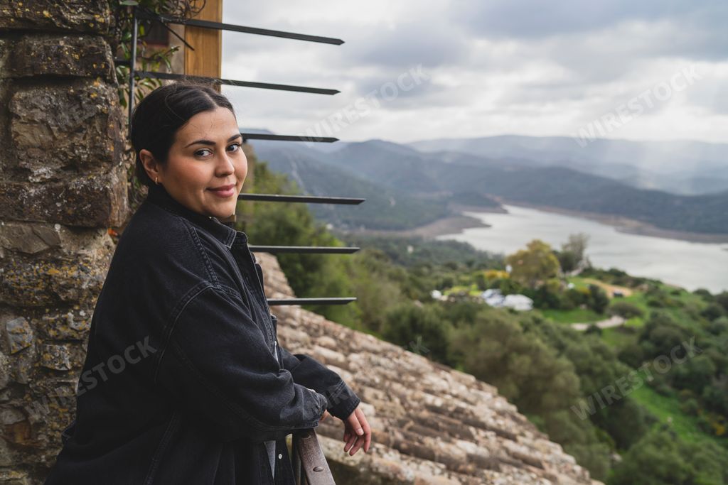 A photo of a Caucasian woman leaning over balcony railing and looking at the camera
