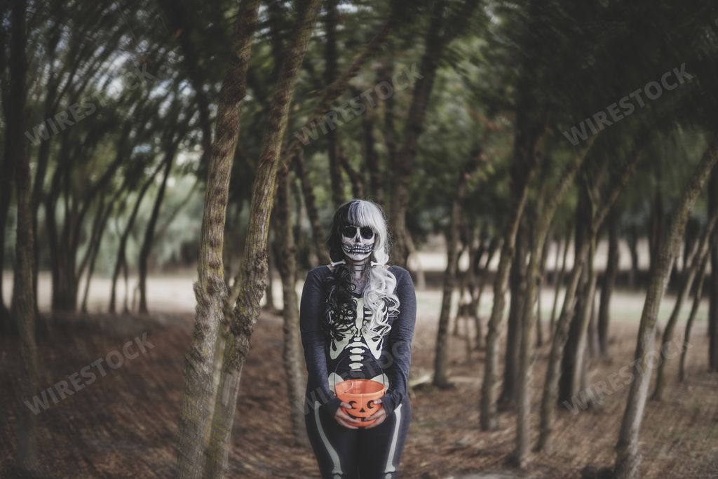 A female wearing a skeleton costume and skull makeup on her face in the middle of a creepy forest