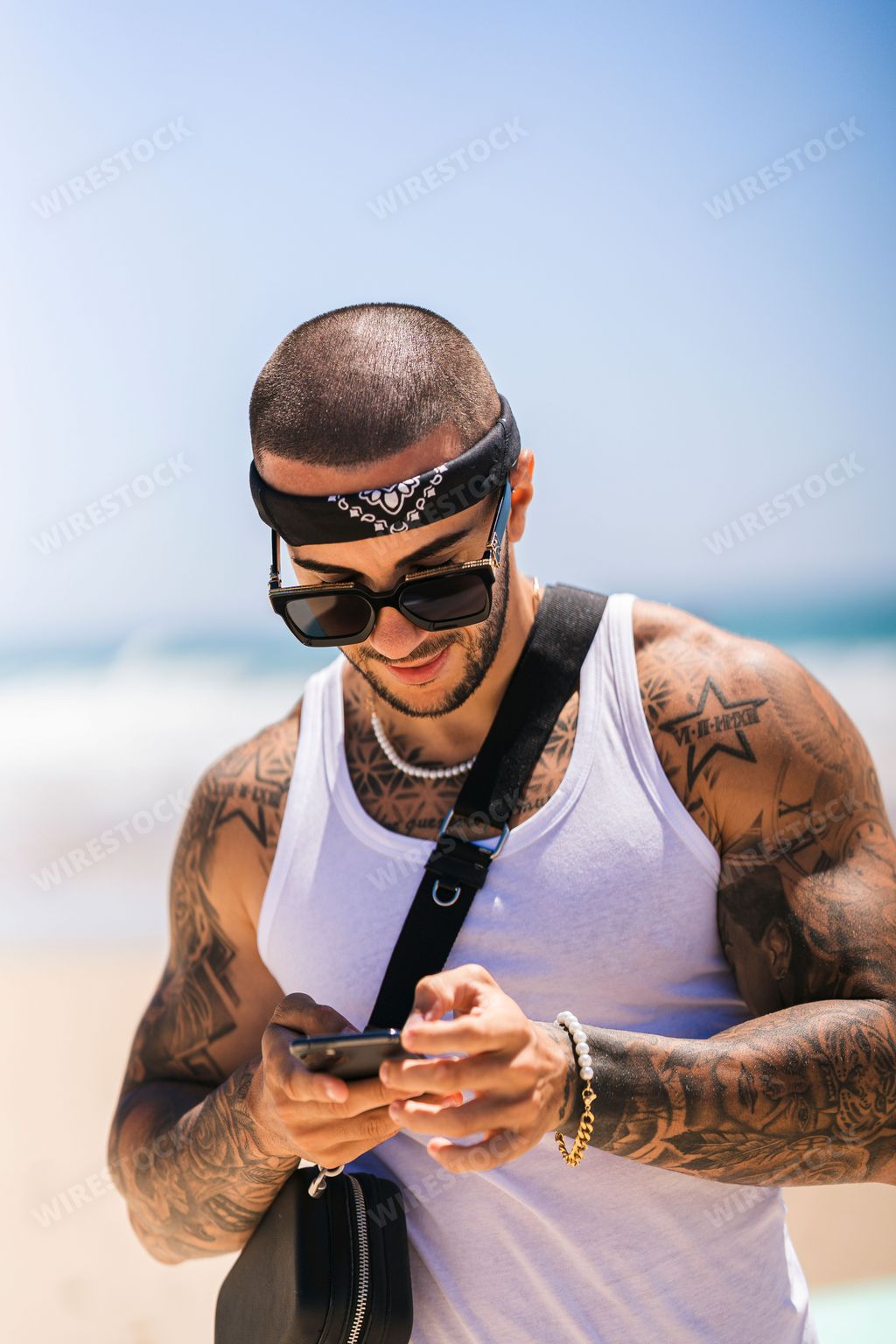 A vertical portrait of an attractive man with tattoos at the beach on a sunny day