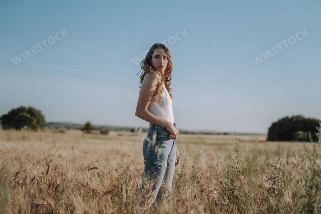 A beautiful blonde Spanish girl looking at the camera in a sunny wheat field under a clear blue sky