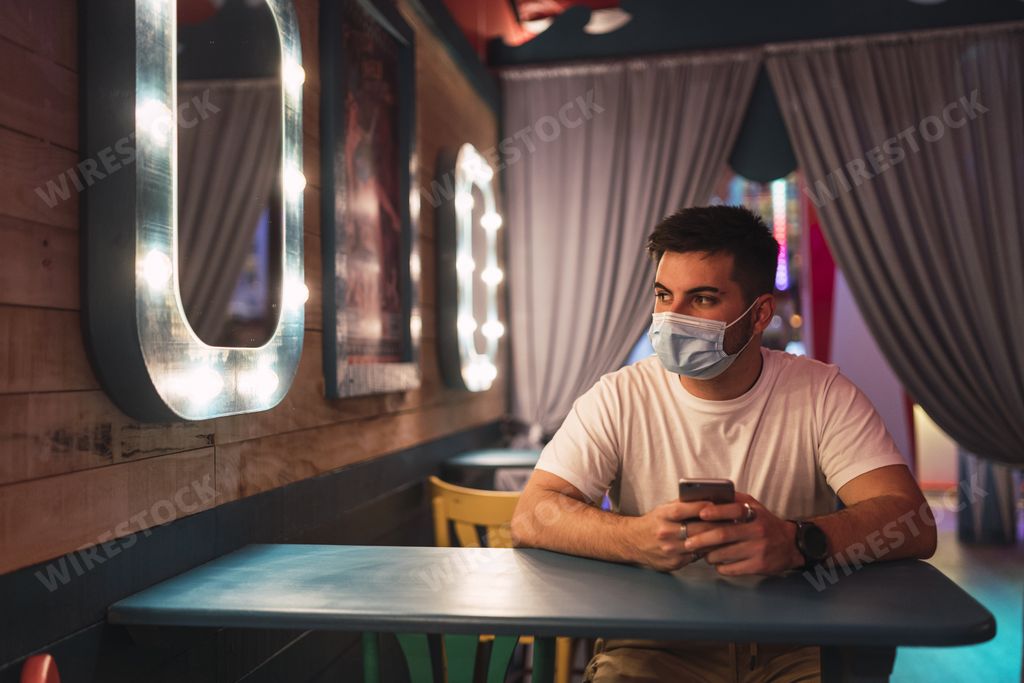 A young Spanish guy wearing a face mask is sitting in a cafe; social life during pandemic