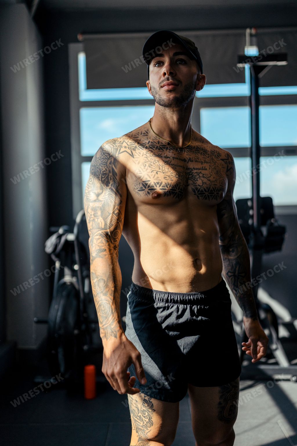 A young, tattooed male with a fit physique poses in a gym