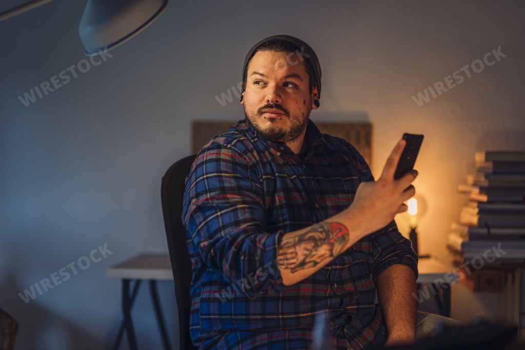 A closeup portrait of a handsome tattooed man with hat taking picture of something while sitting at home