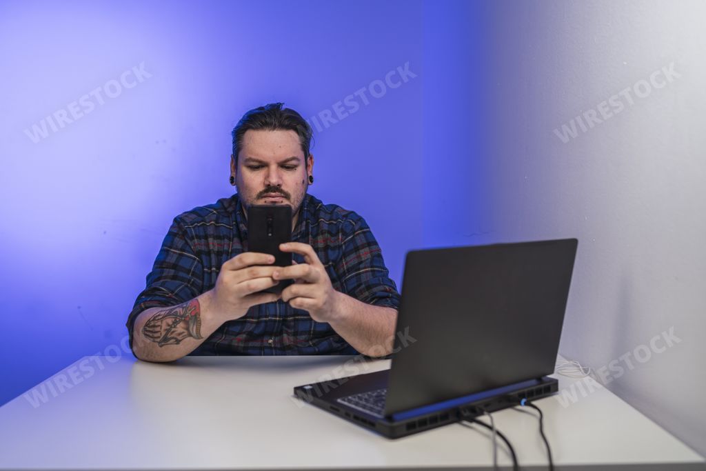 A casual businessman sitting in front of his laptop and busily tapping on his smartphone
