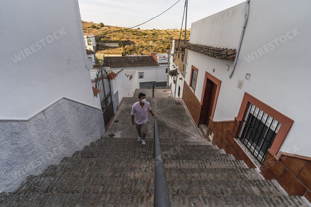 A high angle shot of a young male with a face mask climbing stairs in an old alley in Andalusia, Spain
