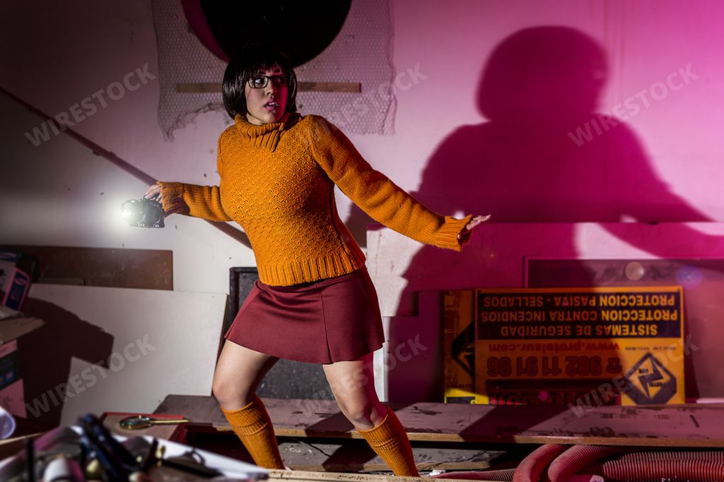 A female wearing makeup and costume like Velma from Scooby-Doo movie standing in an attic