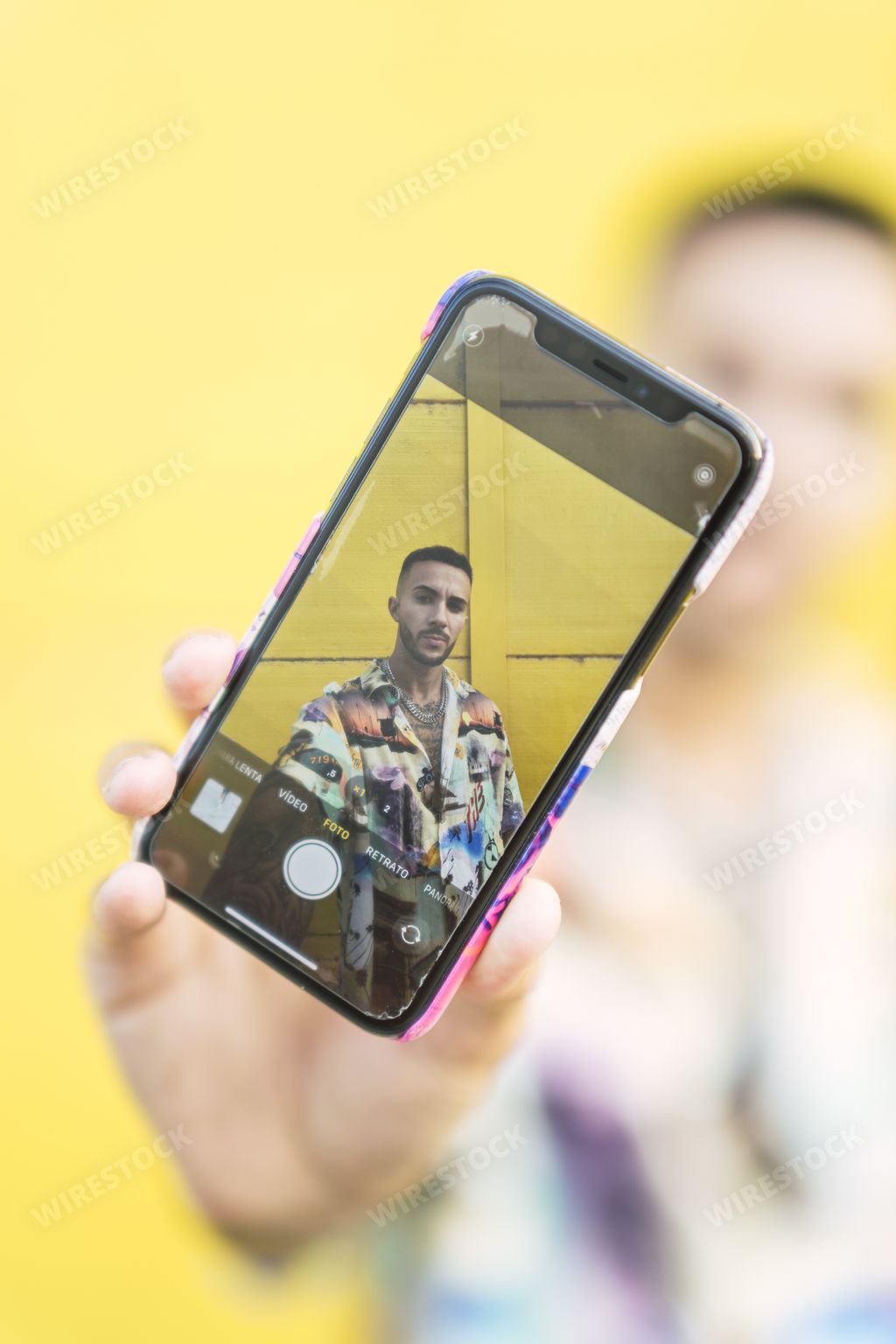 A vertical shot of a handsome male taking a picture of himself by a yellow wall