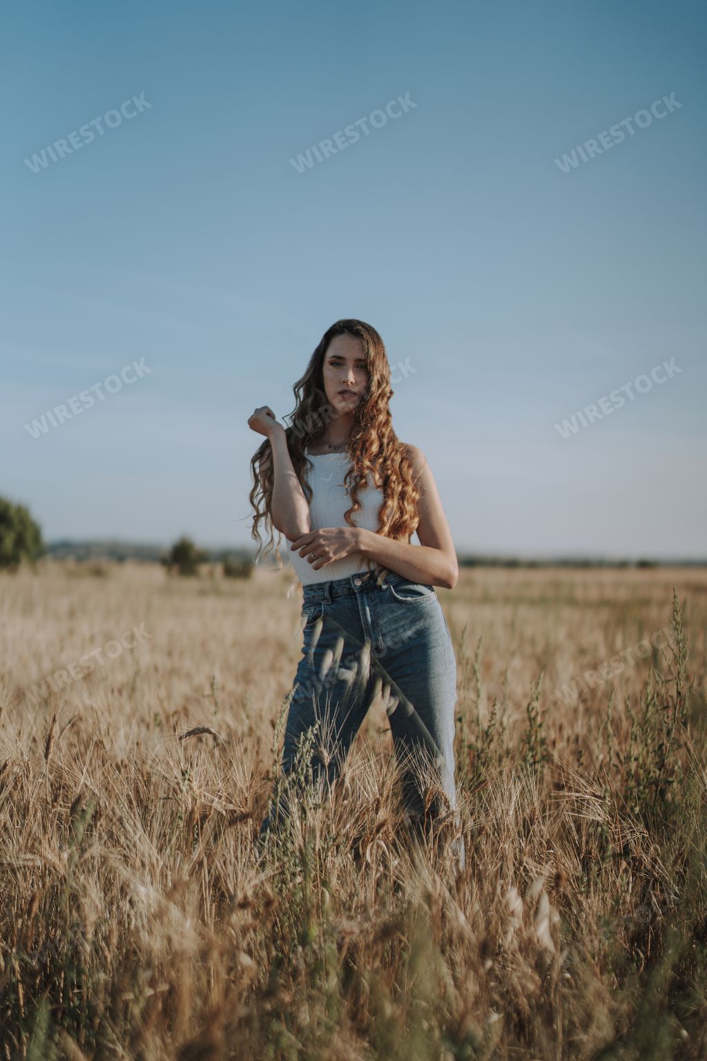 A breathtaking shot of a stunning Spanish girl with curly blond locks looking at the camera in a sunny field