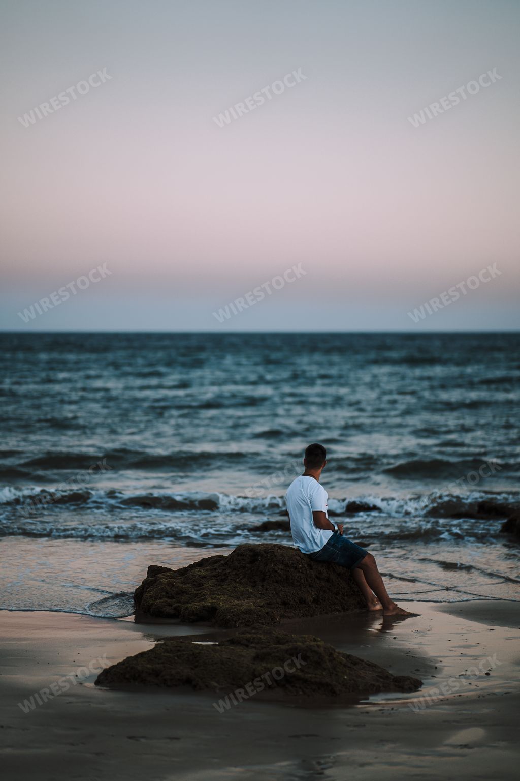 An amazing shot of a man sitting on a beach rock and enjoying a beautiful seascape view