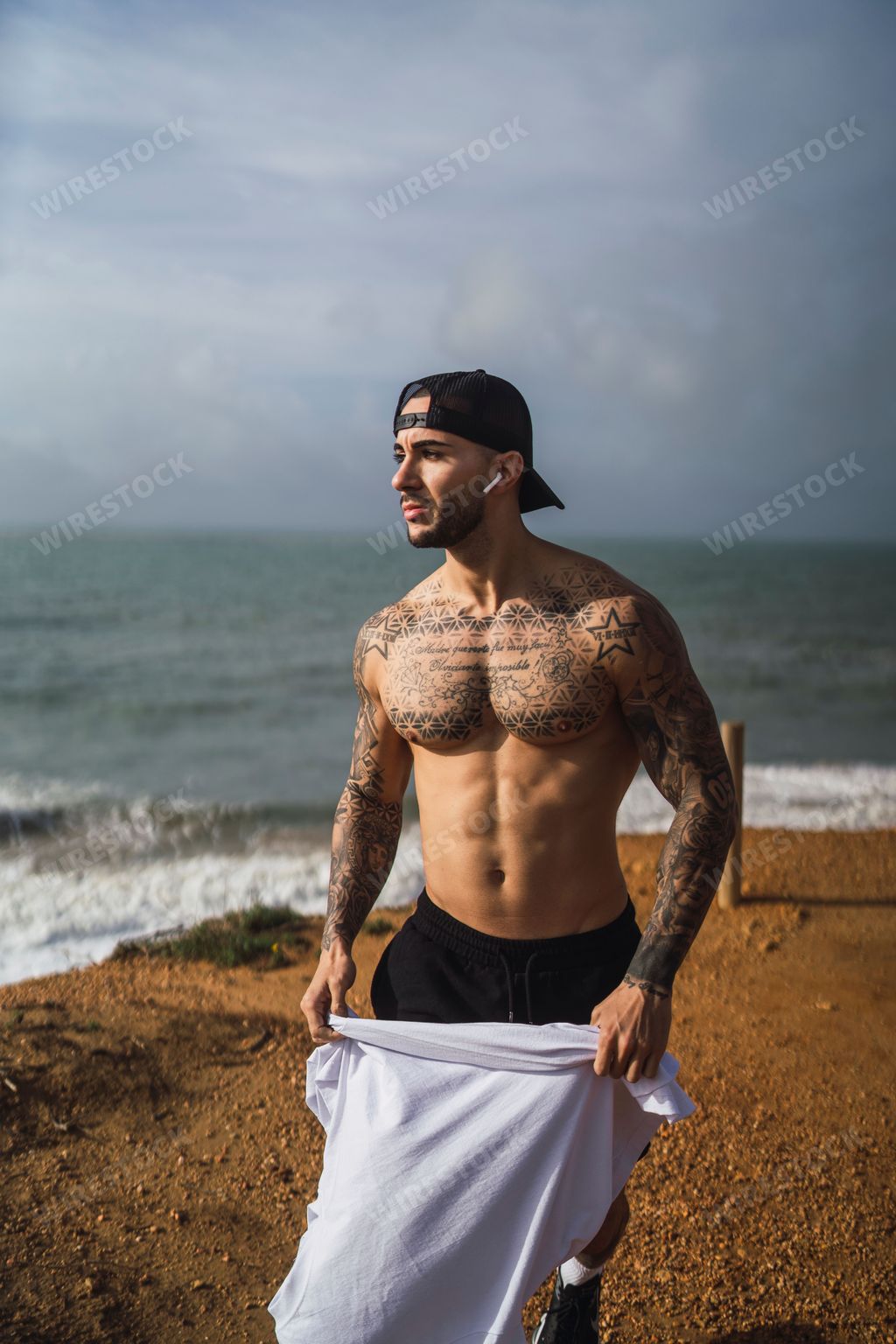 A topless Caucasian man from Spain with tattoos posing in a beach