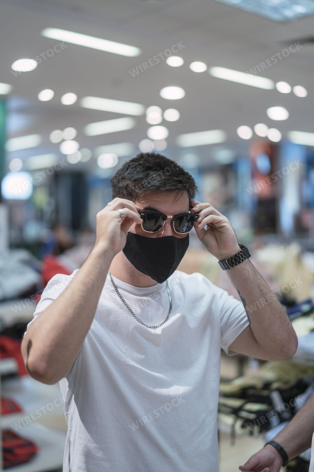 A vertical shot of a stylish young Spanish man trying on sunglasses in the mall