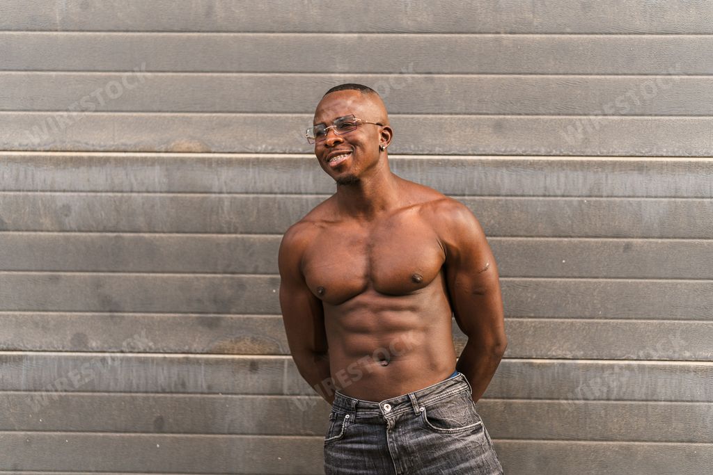 A fit sexy attractive black shirtless male in jeans and sunglasses posing