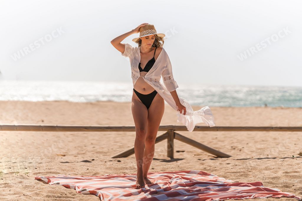A view a young and beautiful Spanish woman in a bikini and white robe posing at the beach