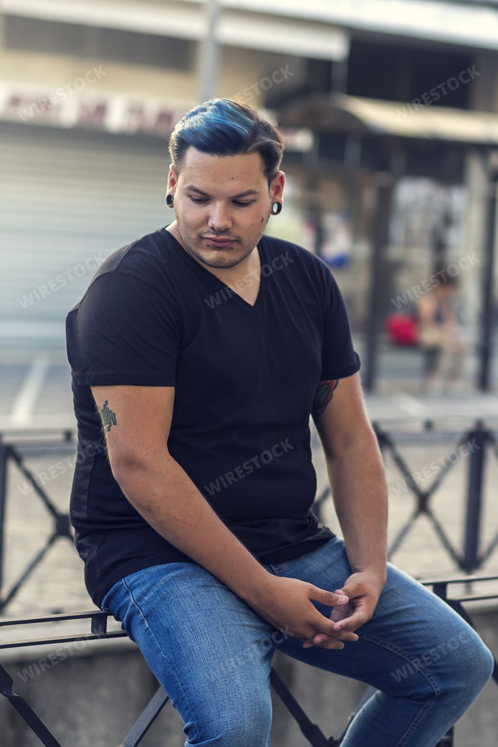 A vertical shot of a Caucasian man with a tattoo on his hand sitting alone - the concept of loneliness