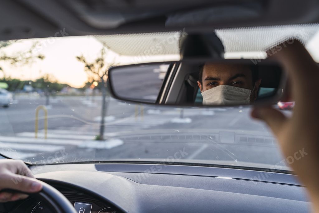 A young Caucasian male driving a car with a medical face mask - the new normal after Covid-19