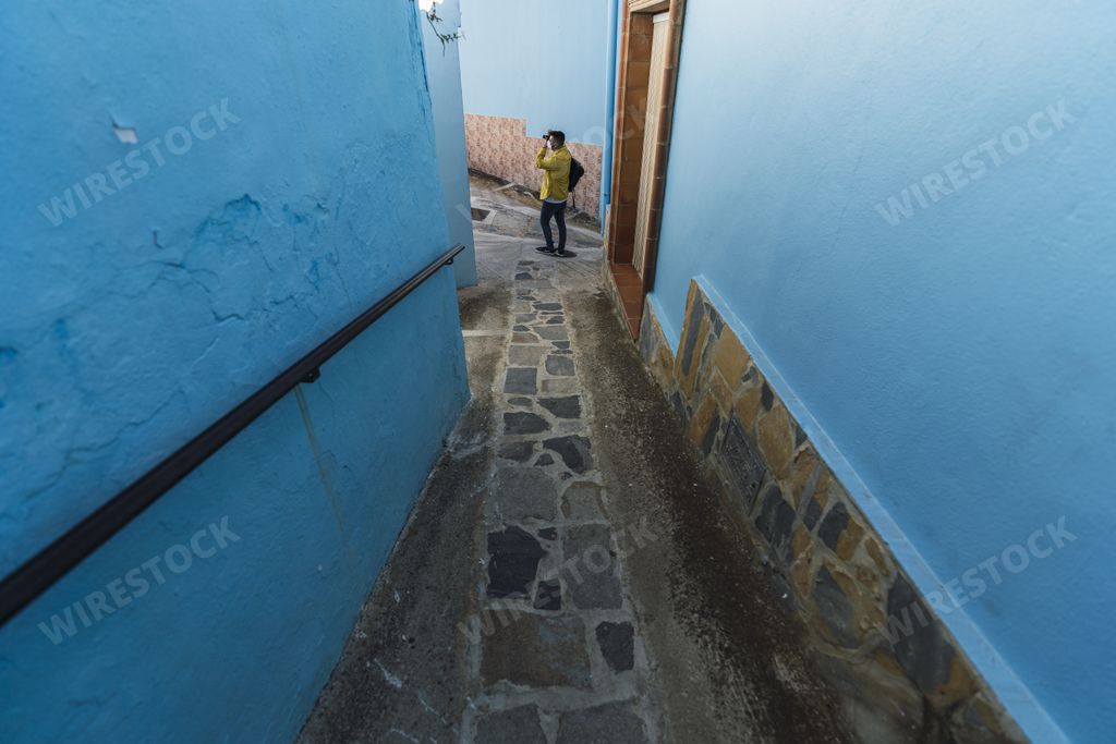 A male wearing a yellow jacket while standing in a narrow alley