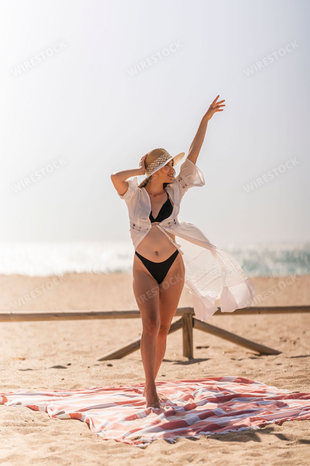 A vertical shot of a young and beautiful Spanish woman in a bikini and white robe posing at the beach