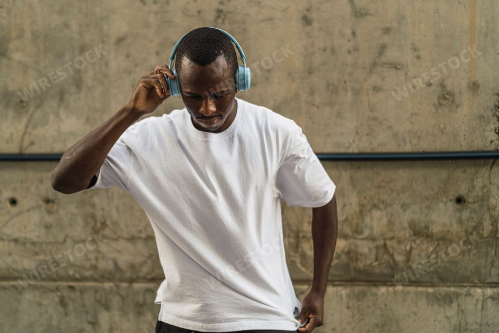 A young cool black male in a street style outfit listening to music with blue headphones outdoors