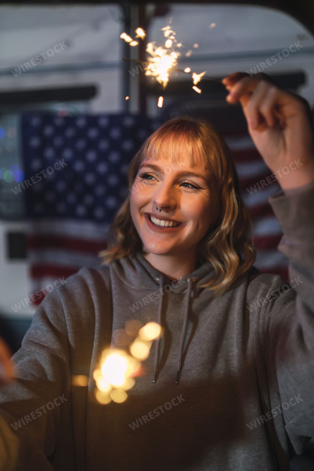 A portrait of a young Spanish female holding bengal sparklers on background of US flags at night